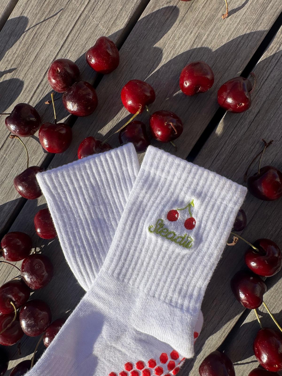 Beautiful Premium Reformer Pilates Sock with Cherry Design, sitting on a bed of cherries with the sunlight pouring in